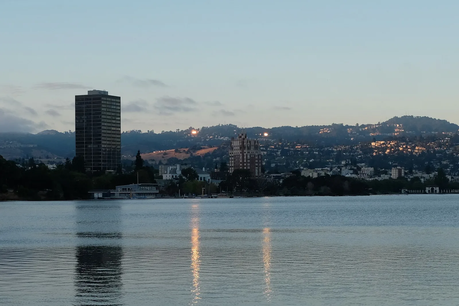 Lake Merritt at dusk with houses climbing the Oakland Hills behind the shoreline