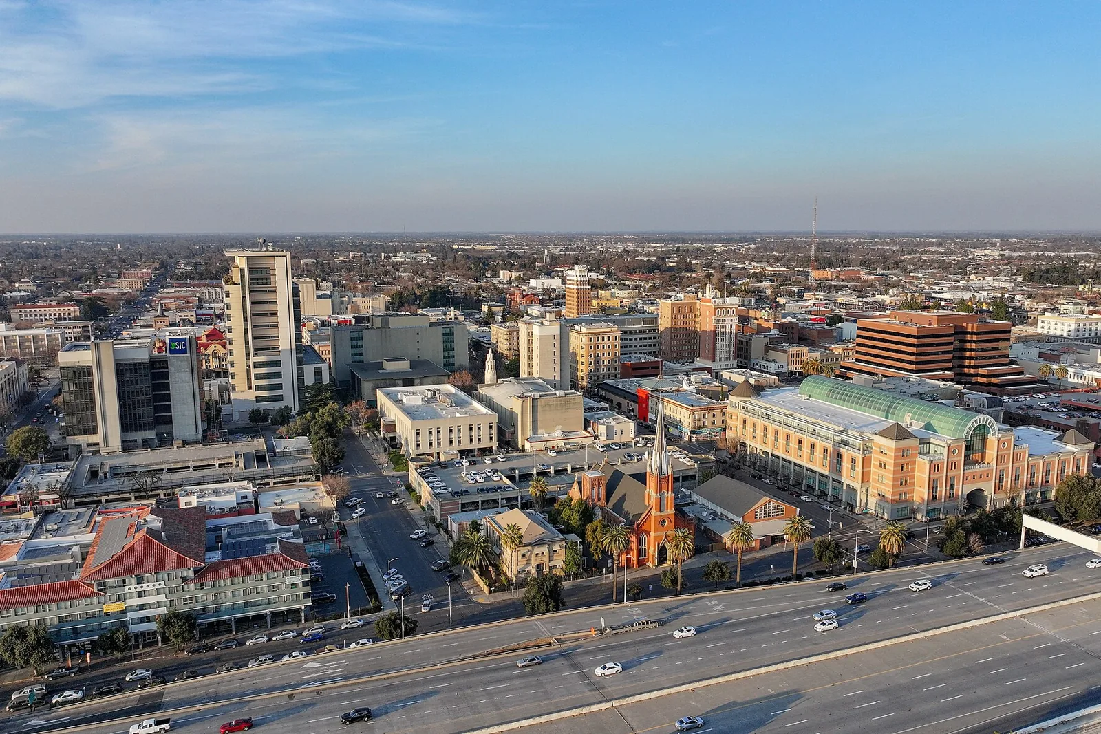 Aerial view of downtown Stockton, California, with the Cathedral of the Annunciation spire and Interstate 5 in the foreground under a clear sky