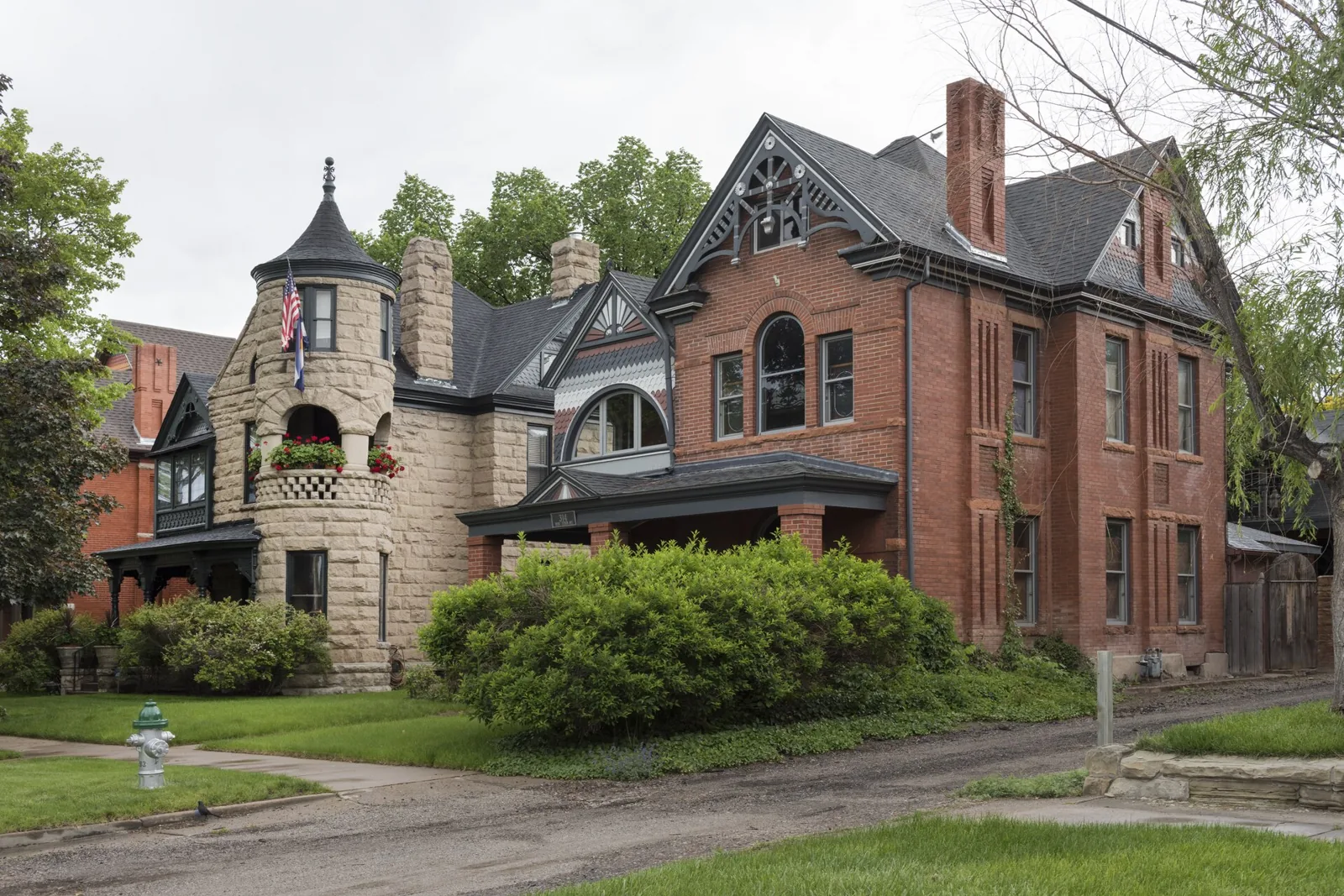A sandstone Victorian house with a corner turret beside a brick Queen Anne in the Pitkin Place historic district of Pueblo