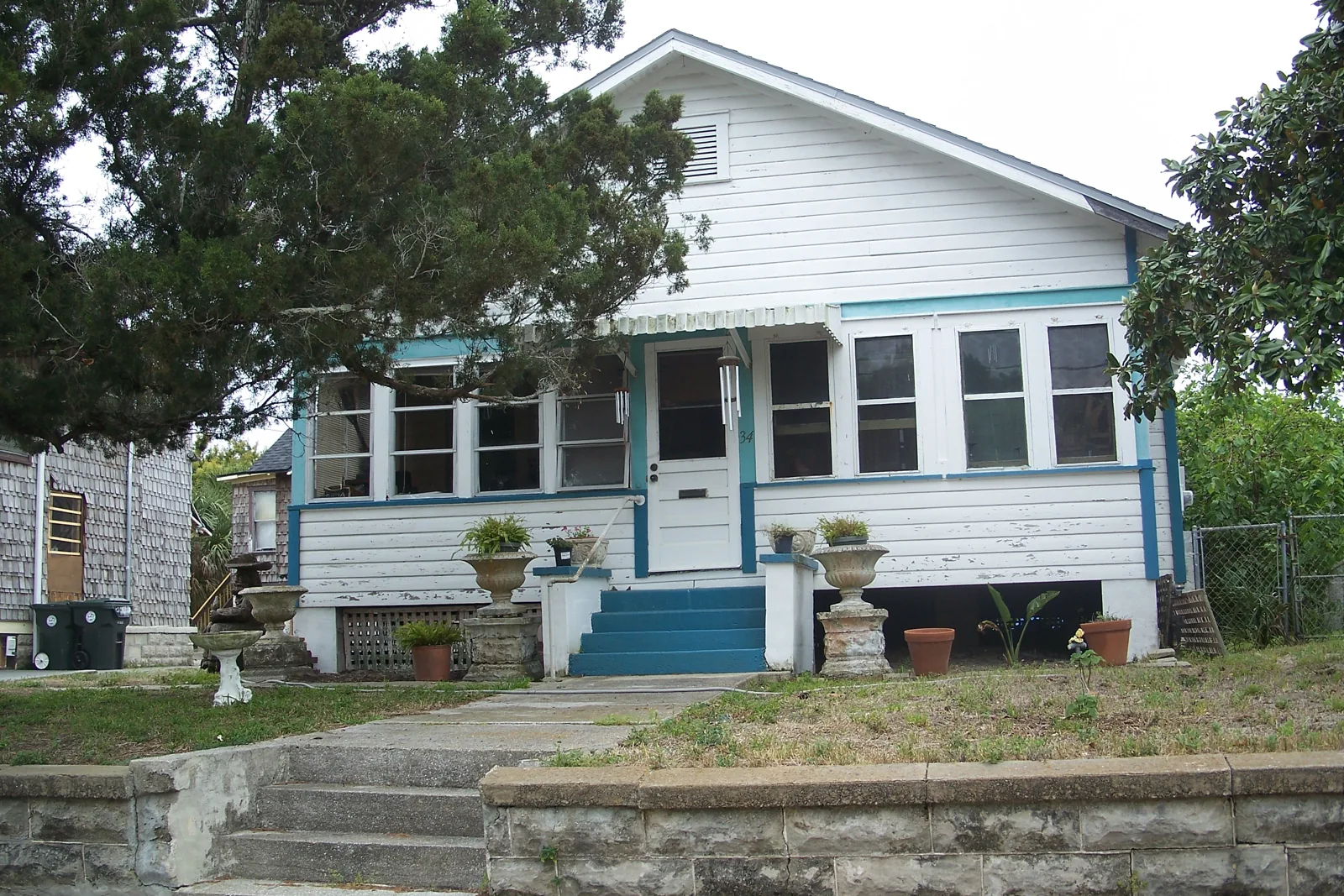 White wood-frame bungalow with a blue-trimmed porch behind a coquina wall in the Surfside historic district of Daytona Beach