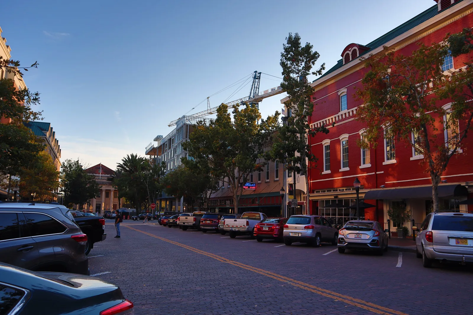 Red brick storefronts and parked cars along a brick-paved street in downtown Gainesville at sunset