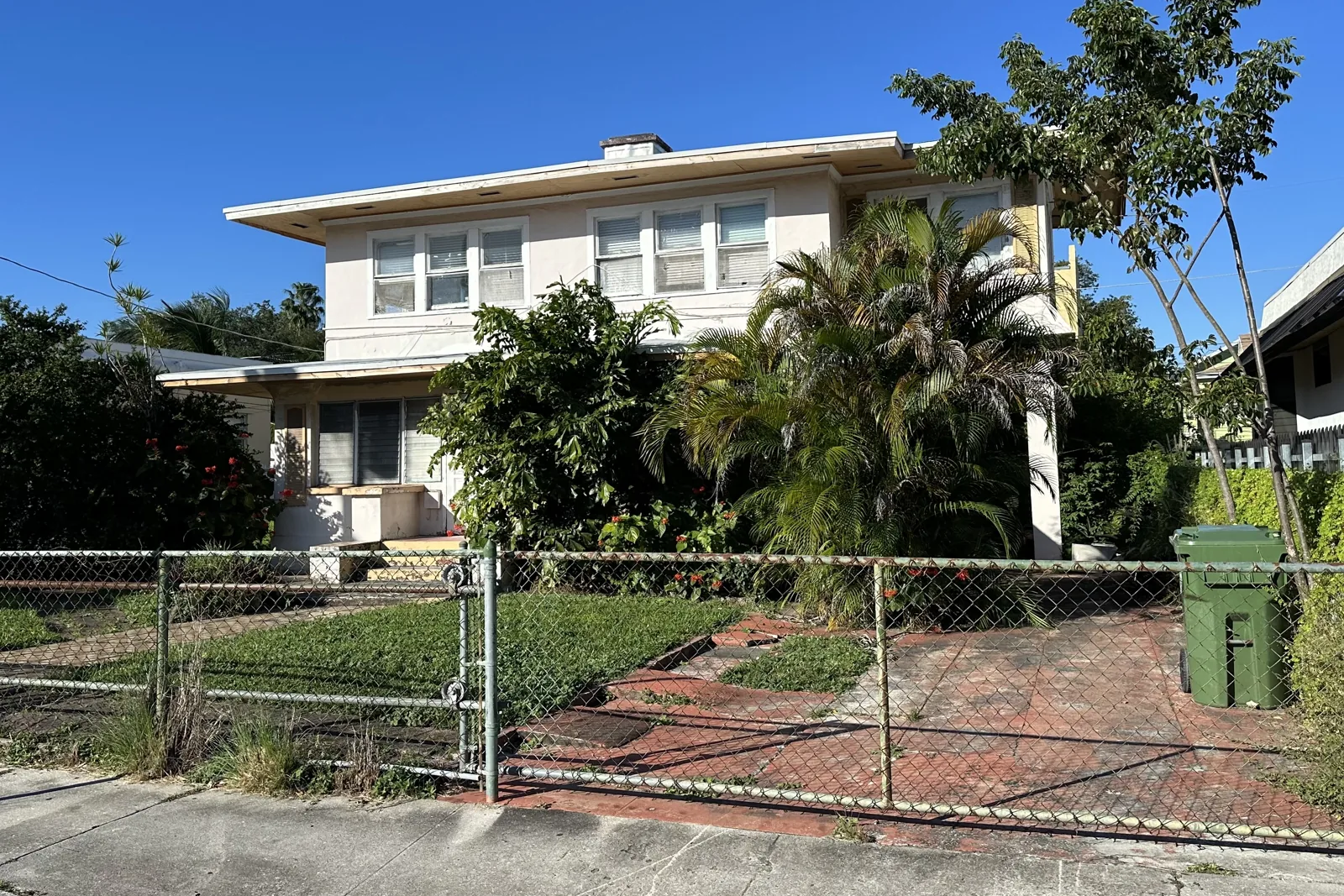 Older two-story house with a chain-link fence and palms on a residential street in Little Havana, Miami