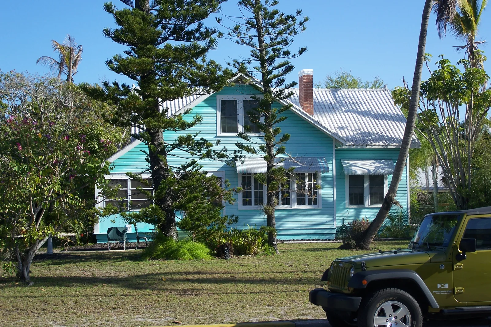 Turquoise wood-frame cottage with a metal roof and Norfolk pines in the Old Naples historic district