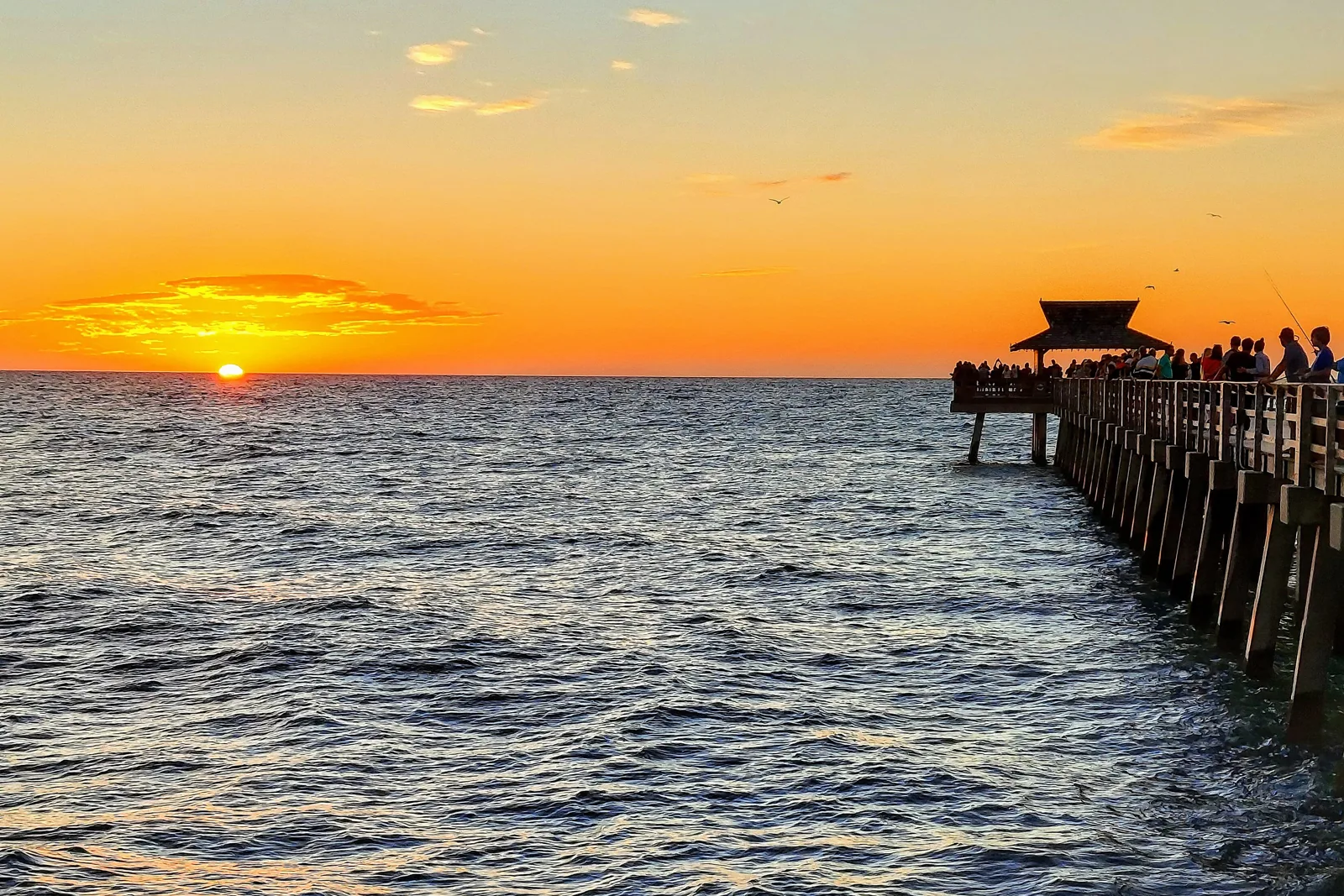 Naples Pier at sunset with people fishing at the end of the pier over the Gulf of Mexico