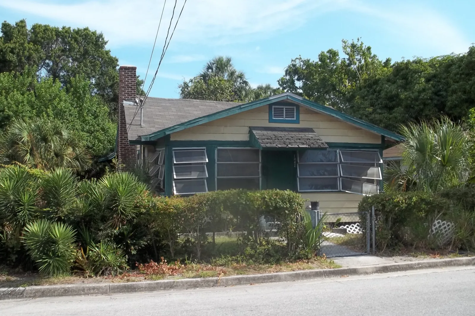 Yellow wood-frame bungalow with jalousie windows and a brick chimney in the Overtown historic district of Sarasota