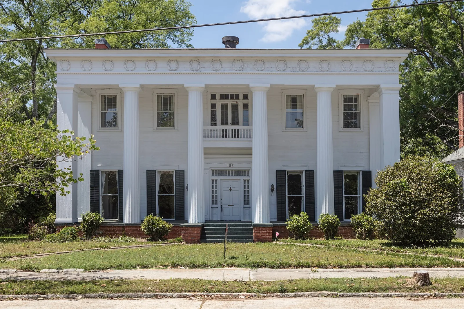 A white Greek Revival house with two-story columns and dark shutters on a residential street in Macon