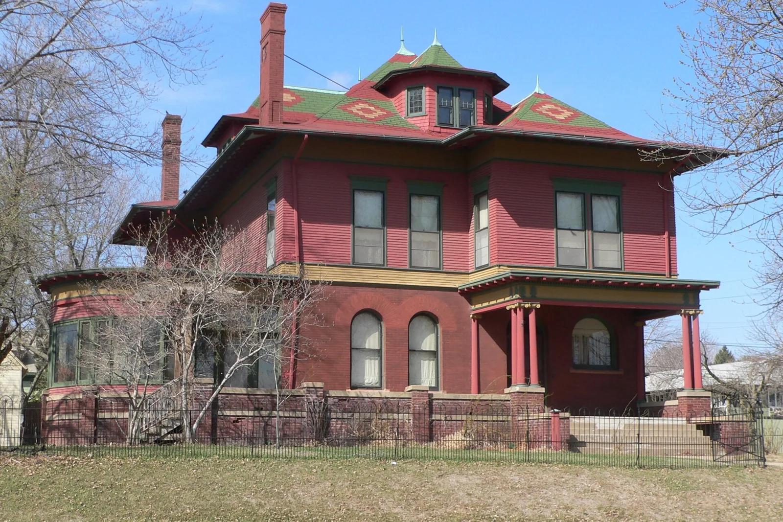 The Burkam house in Sioux City, a red Queen Anne with green trim, a corner tower, and an iron fence under a blue sky
