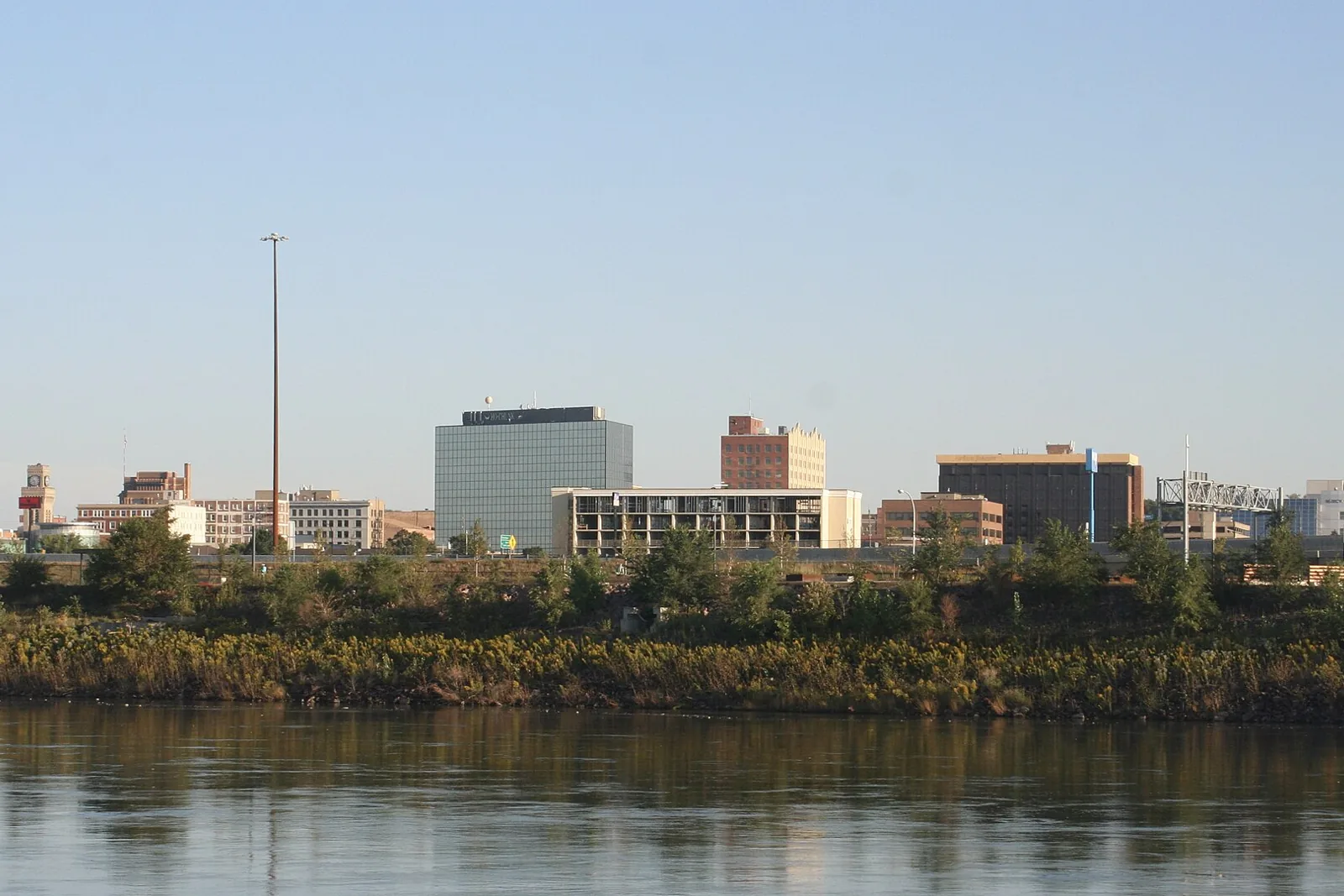 The downtown Sioux City skyline across the Missouri River on a clear morning, with the riverbank brush in the foreground