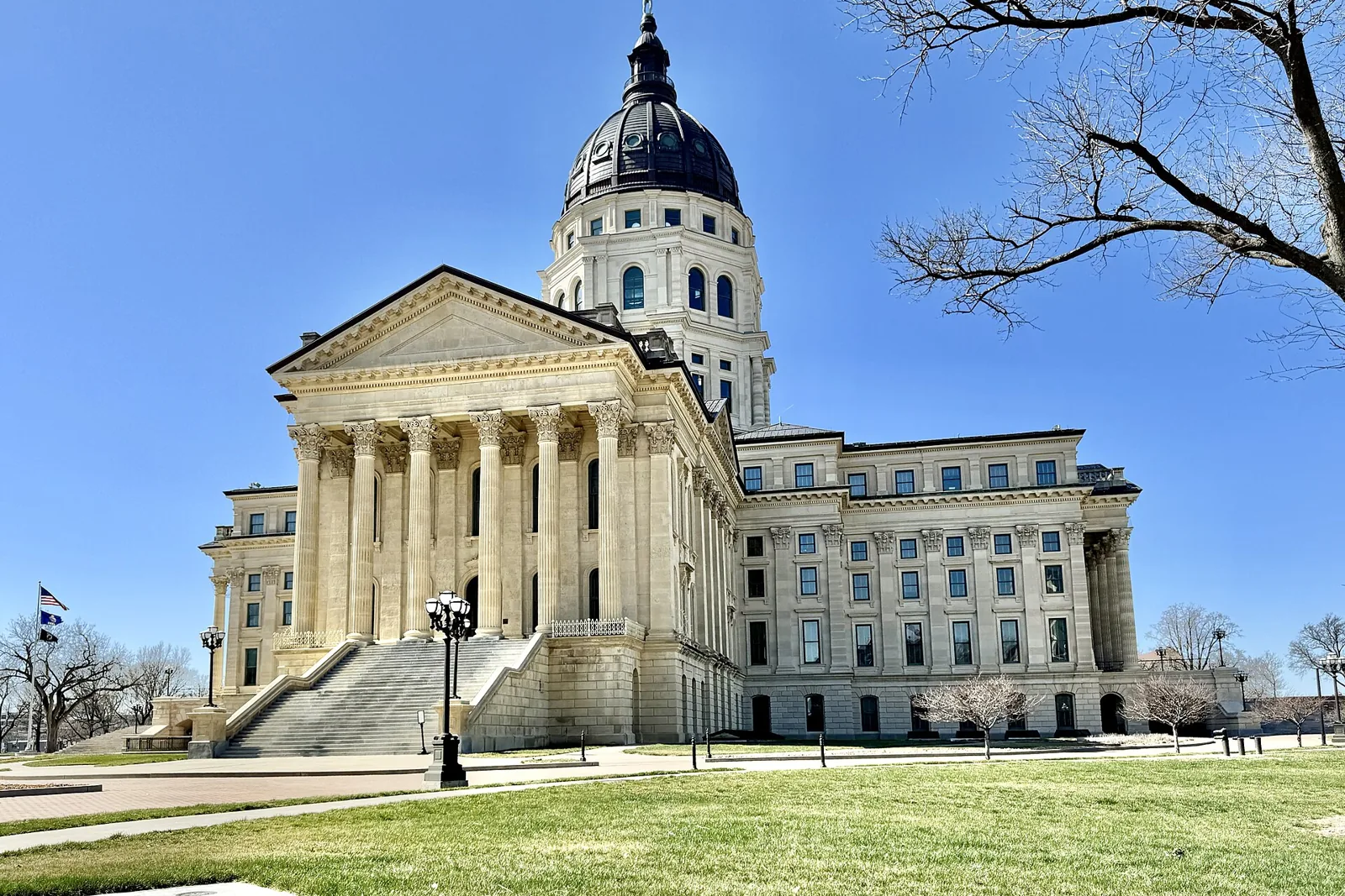 The Kansas State Capitol in Topeka, its limestone portico and dark copper dome under a clear blue sky