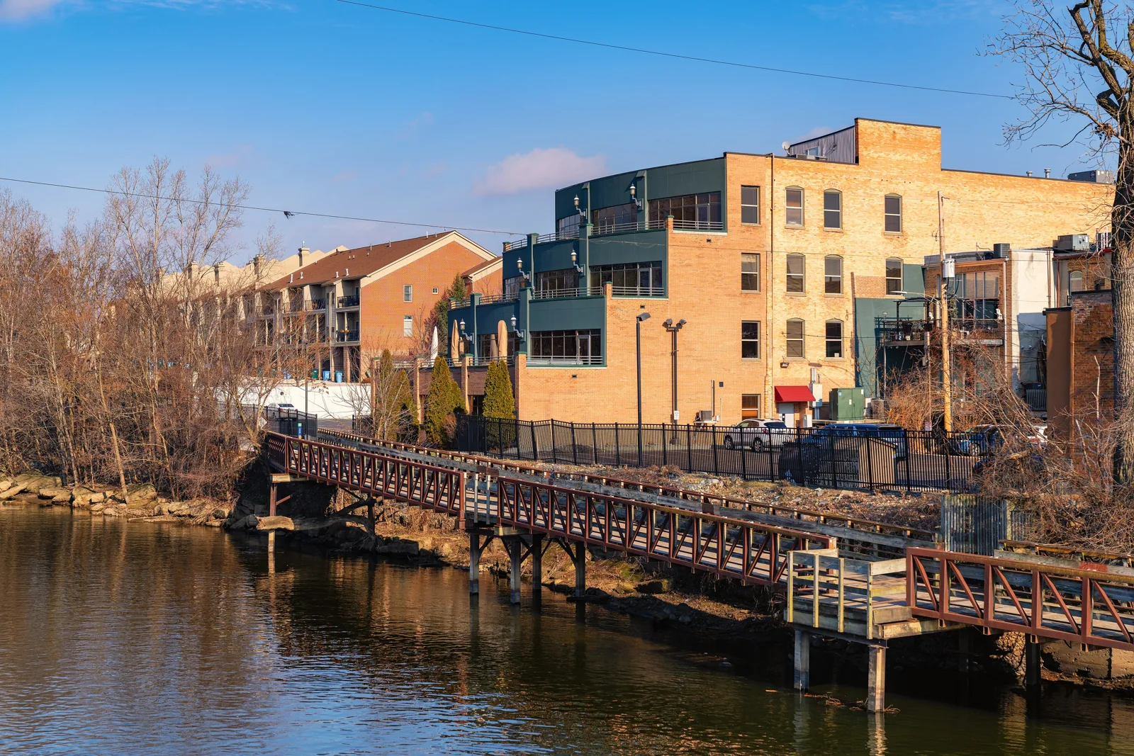 The Lansing River Trail footbridge on the Grand River beside brick buildings in Old Town Lansing