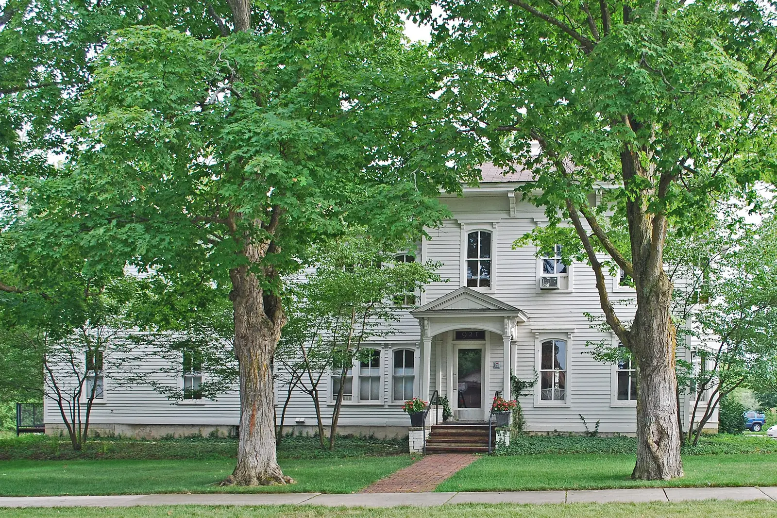 A white two-story Italianate house shaded by maple trees on the former Northern Michigan Asylum grounds in Traverse City