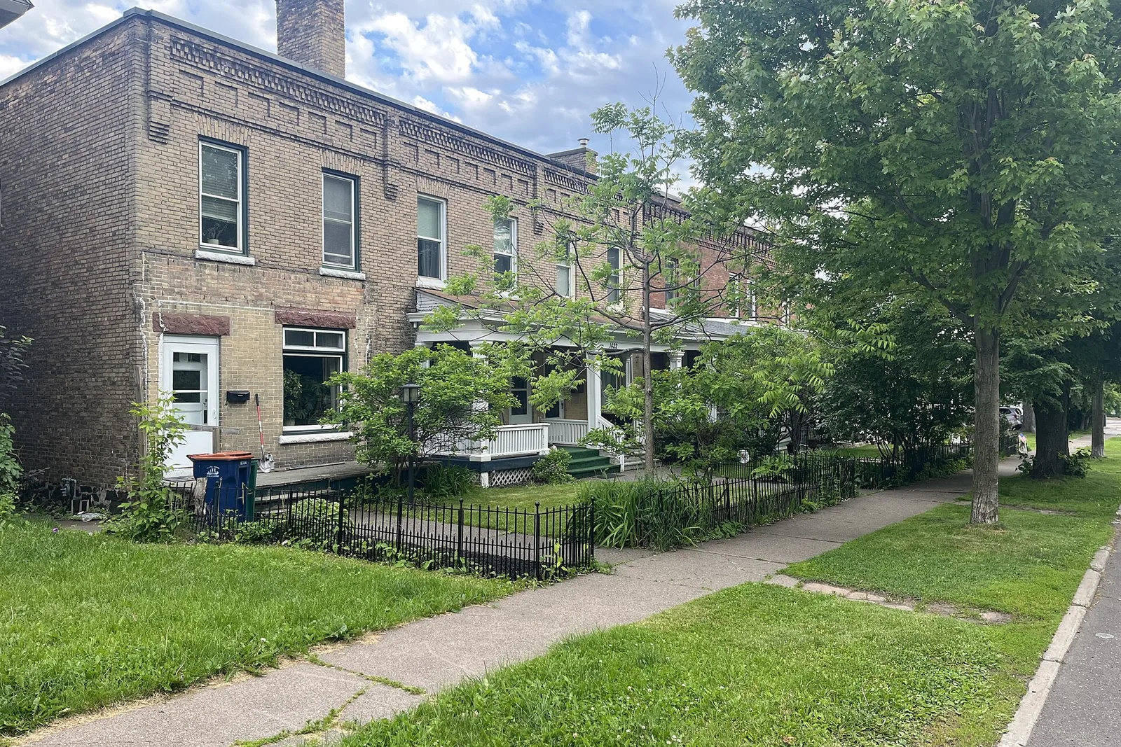 A row of two-story tan brick houses with front porches and iron fences on a tree-lined Duluth street in summer