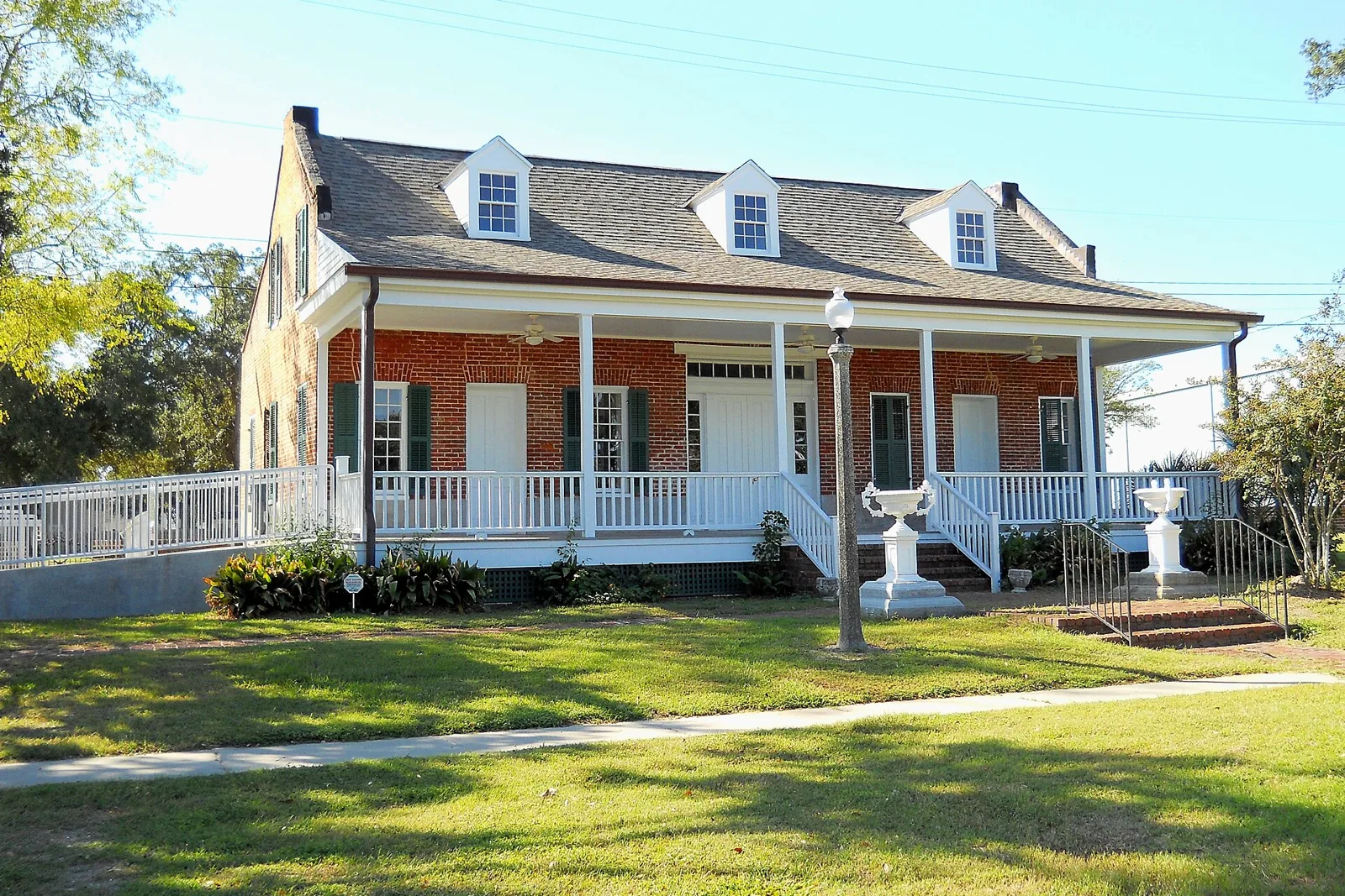 The Old Brick House, a raised brick cottage with a white porch and dormers, on Bayview Avenue in Biloxi under a clear sky