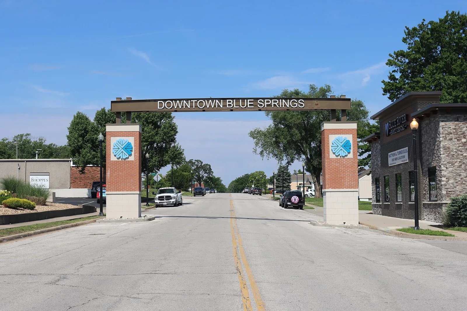 The Downtown Blue Springs gateway arch with two brick pillars spanning the main street in Blue Springs, Missouri, under a clear blue sky