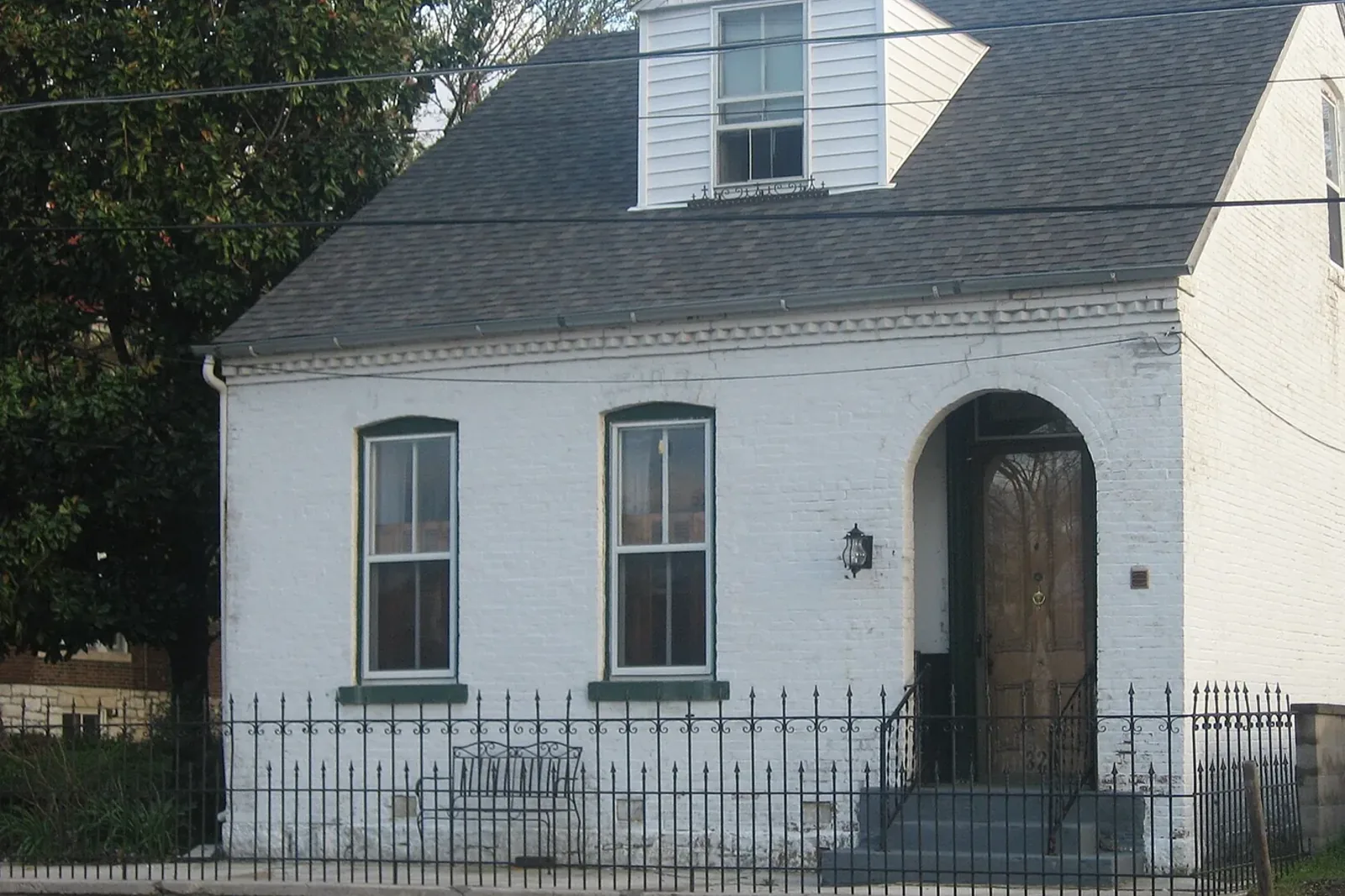 A whitewashed brick cottage with an arched doorway, green trim, and an iron fence on Themis Street in Cape Girardeau
