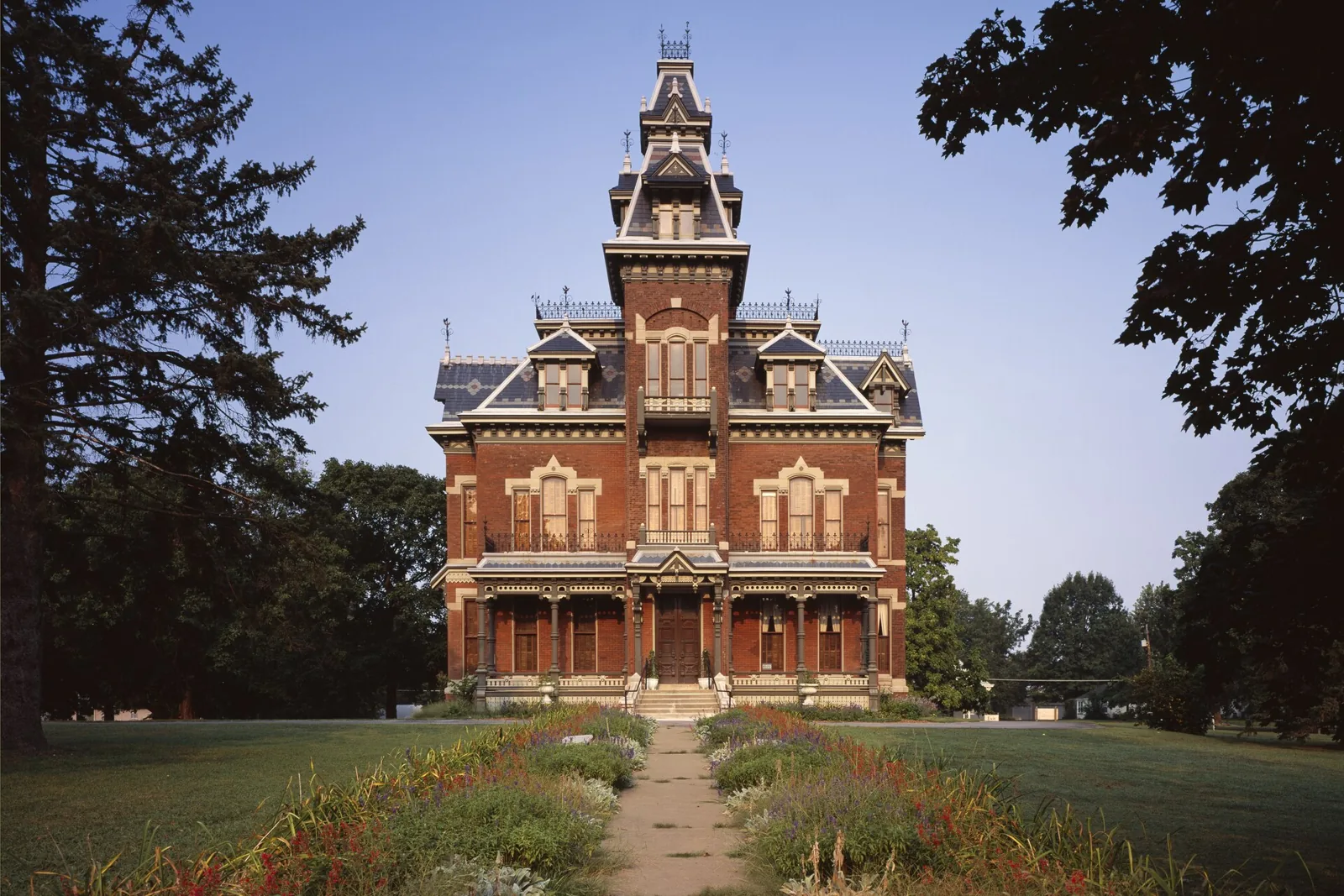 Red-brick Second Empire Vaile Mansion with a mansard roof and tower, seen across a flower-lined walk in Independence, Missouri.