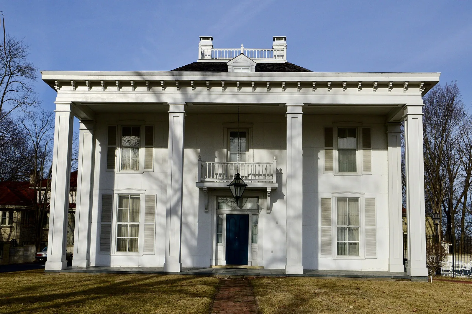 White two-story Greek Revival John C. Edwards House with tall columns and a blue front door on Moreau Drive in Jefferson City, Missouri.