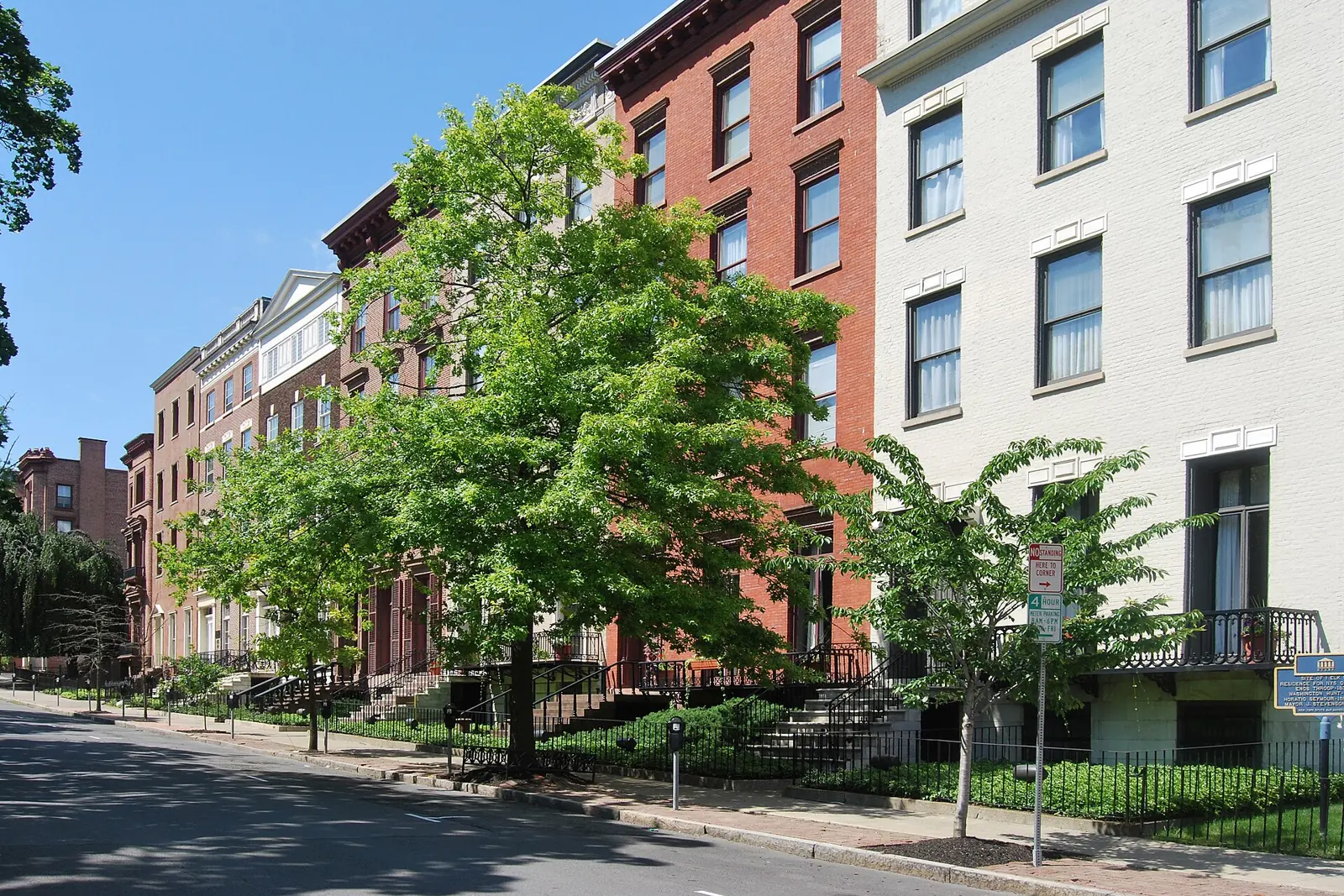 Brick and painted rowhouses with iron railings along Elk Street in Albany under a blue sky