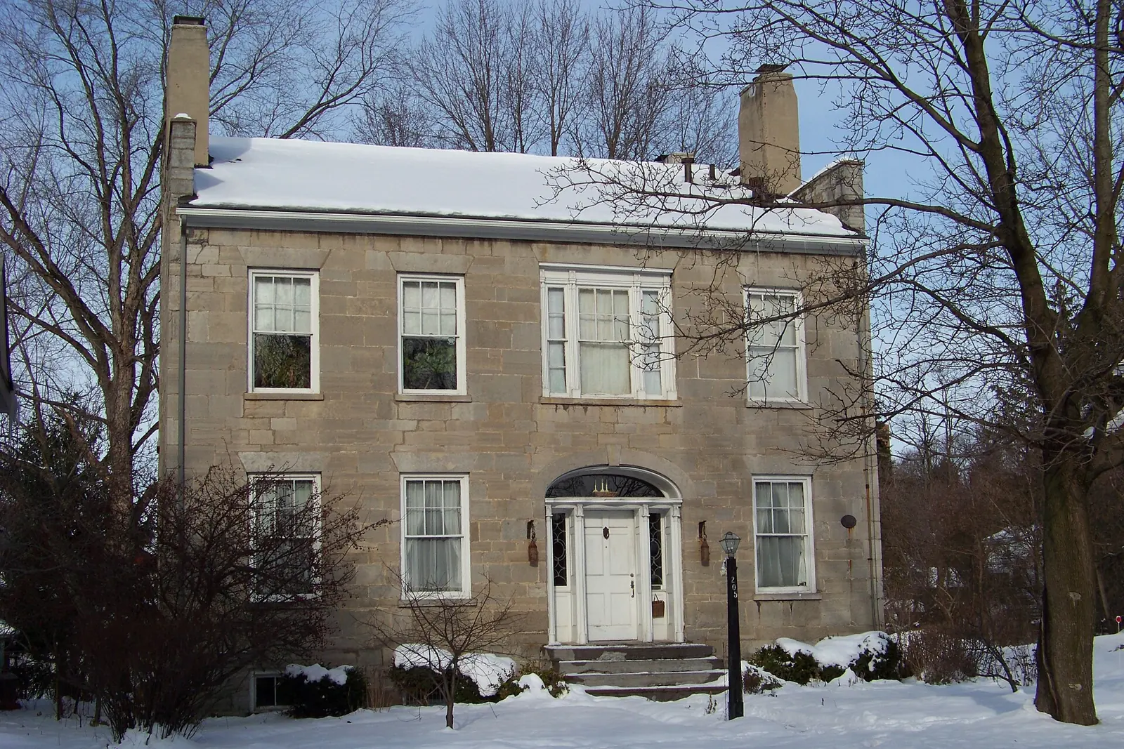 The stone Gridley House on a snowy winter day in Syracuse, framed by bare trees