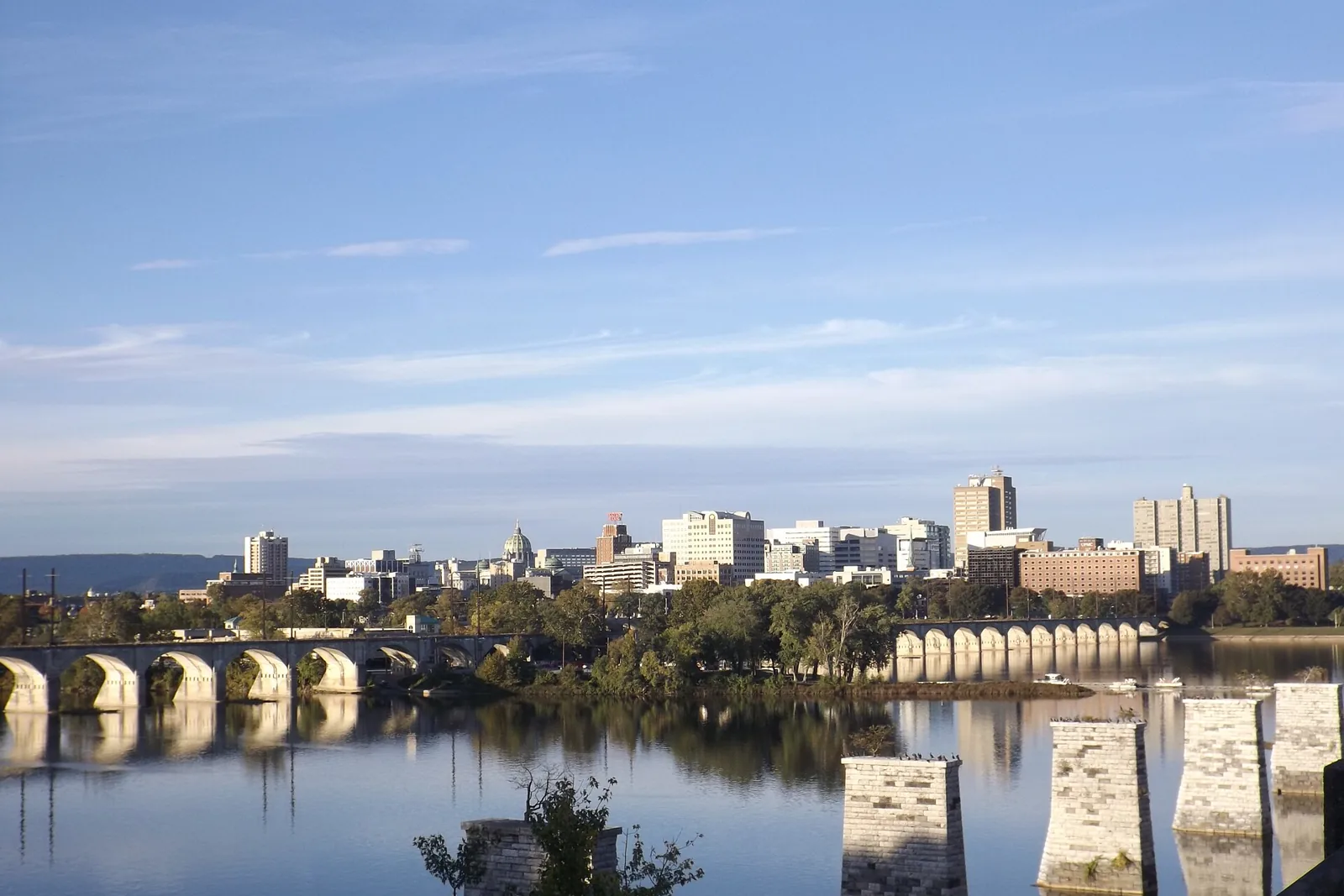 The Pennsylvania State Capitol dome and the downtown Harrisburg skyline above the Susquehanna River and its stone arch bridges on a clear day