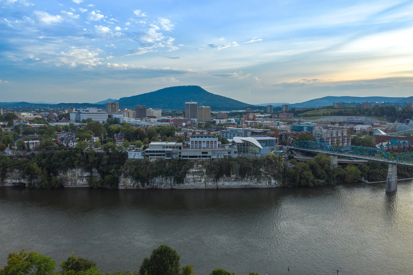 Downtown Chattanooga skyline seen across the Tennessee River from the bluffs, with Lookout Mountain behind and the Walnut Street Bridge at right