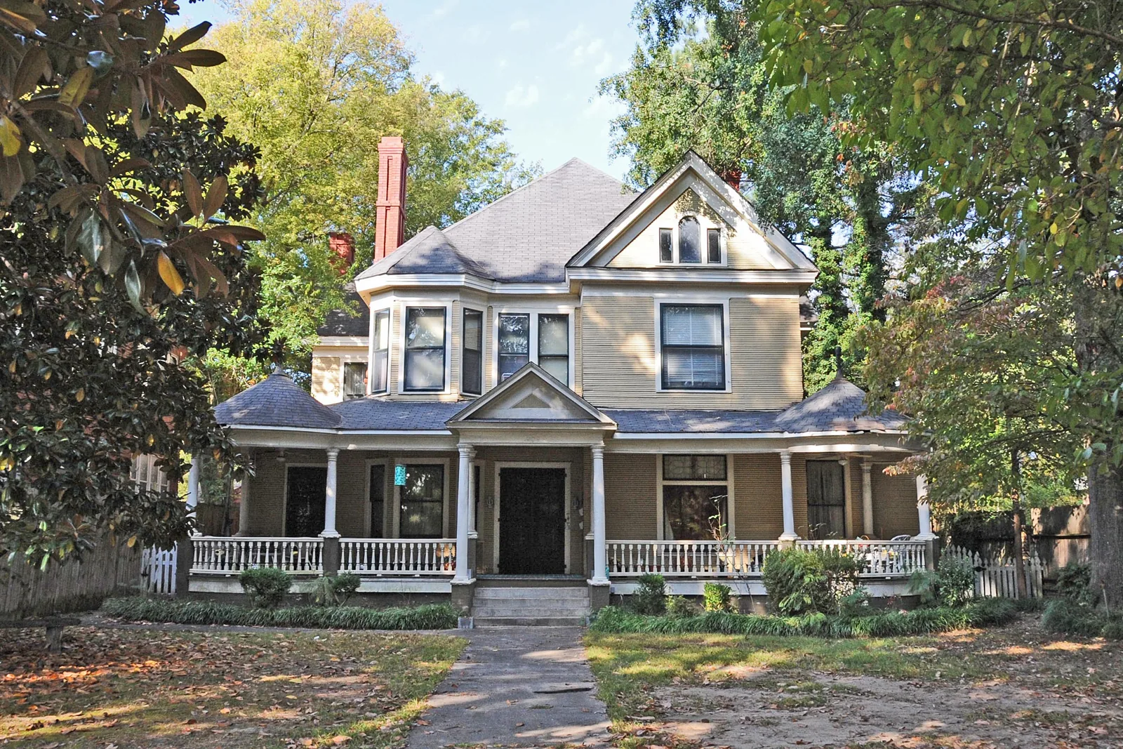 Two-story Queen Anne house with a wraparound porch and a bay turret behind a magnolia tree in Jackson, Tennessee