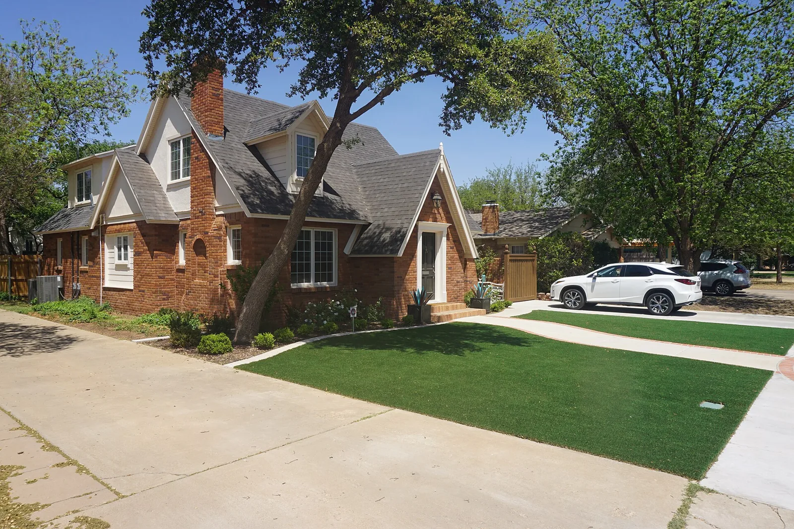 A brick Tudor Revival house with a steep gabled roof and a shade tree on 20th Street in Lubbock