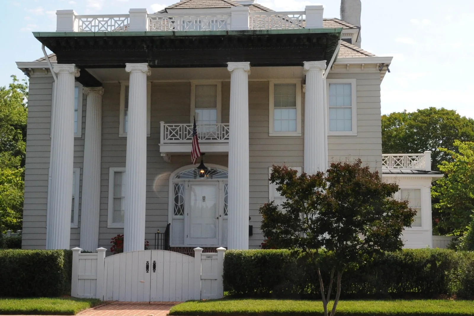 A two-story house with tall fluted columns, a balcony, and a white garden gate in the North End historic district of Newport News