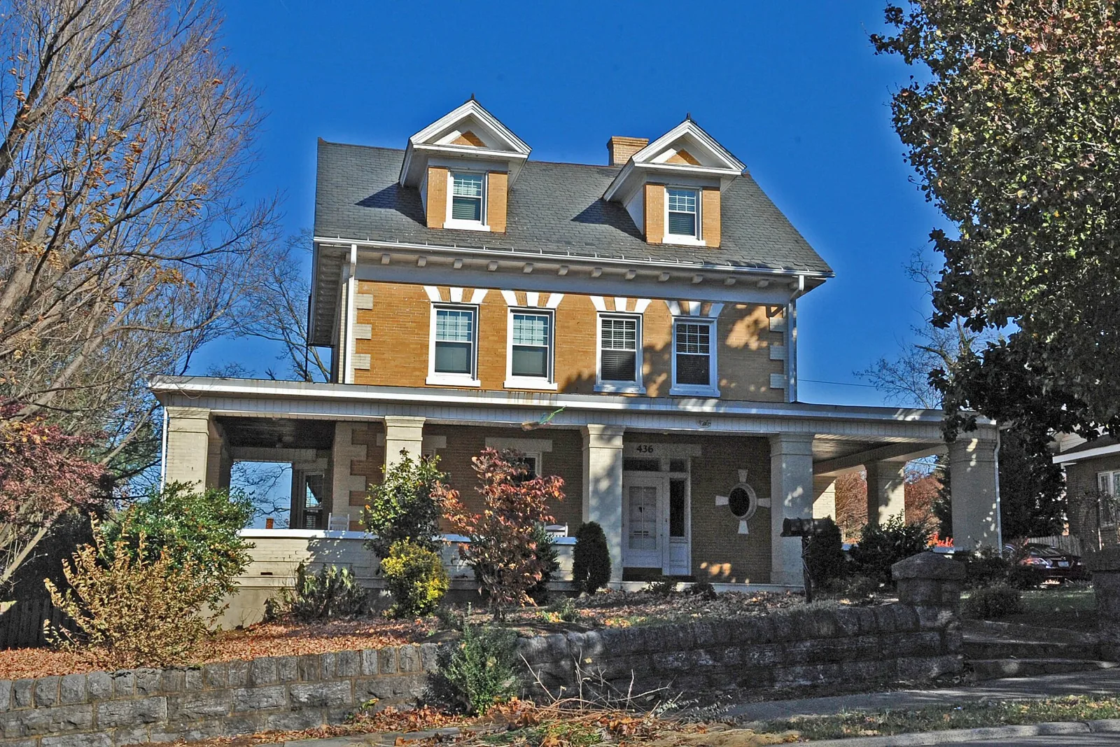 A brick Foursquare house with a wide front porch and a stone retaining wall in the Riverland Historic District of Roanoke