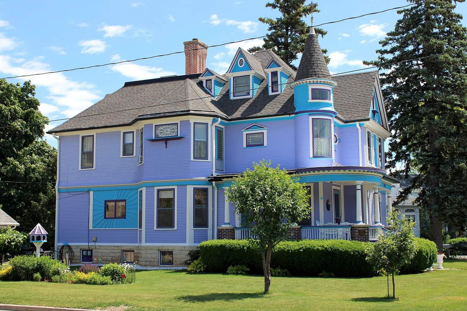 A lavender Queen Anne house with a turret and wraparound porch on a tree-lined street in Appleton