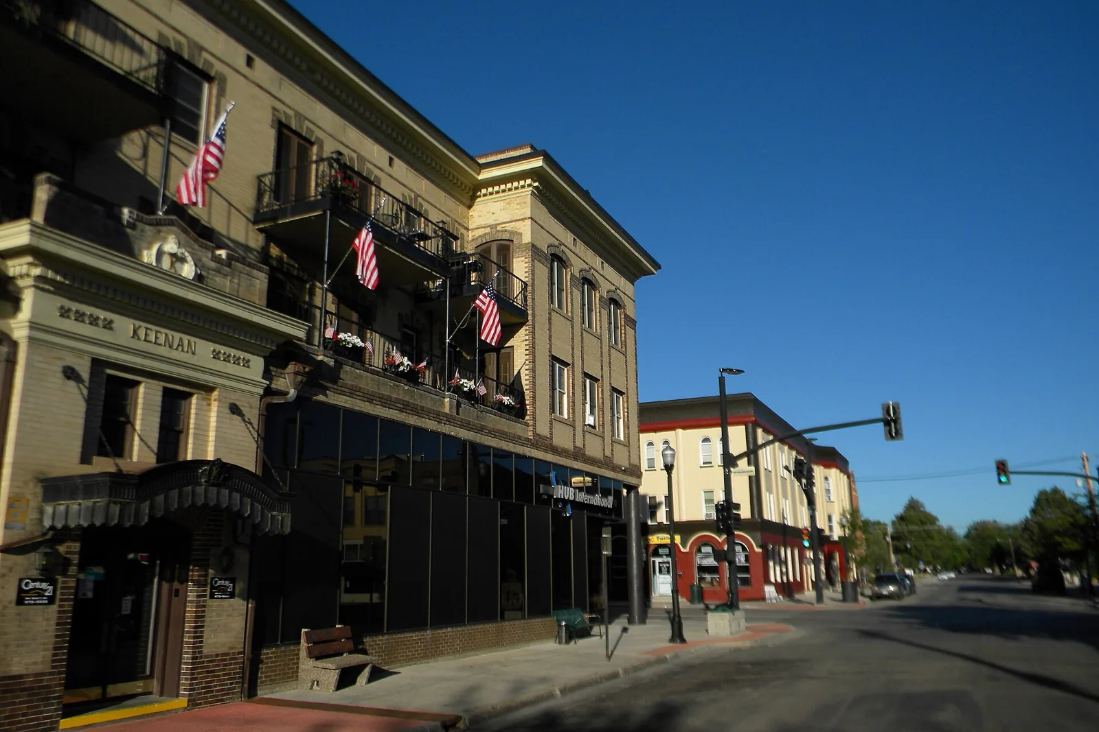 Early-morning view along Main Street in downtown Sheridan, Wyoming, past the historic Keenan building with American flags on its balconies, under a deep blue sky.
